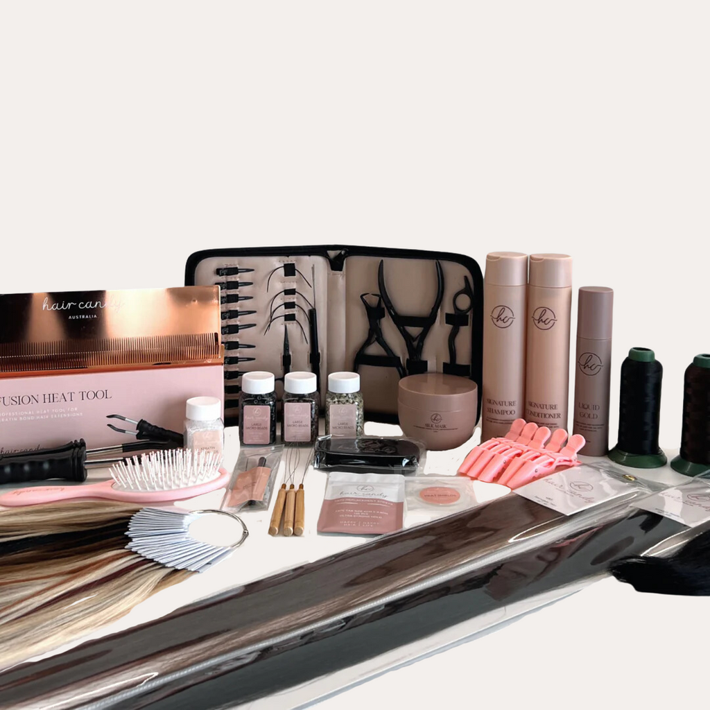 An extensive collection of hair extension tools and accessories laid out on a table, including bottles of micro beads, thread spools, hair grips, wooden threaders, alligator clips, flat clips, practice hair weft, and more.