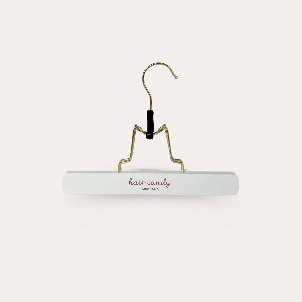 A white hair extension hanger with a gold-colored hook and the brand name 'Hair Candy' printed on the arm.