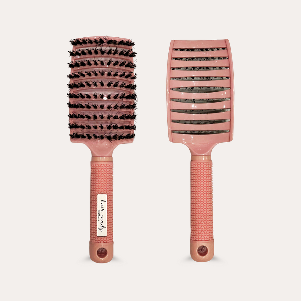A paddle brush with soft bristles and a silicone grip handle with heart detailing, primarily in a pink color.