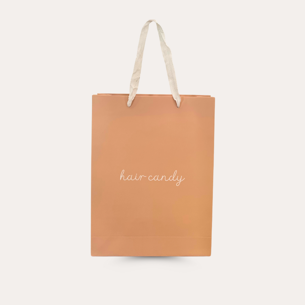 A peach-colored Hair Candy retail bag with the brand name printed in a stylish font on the front.