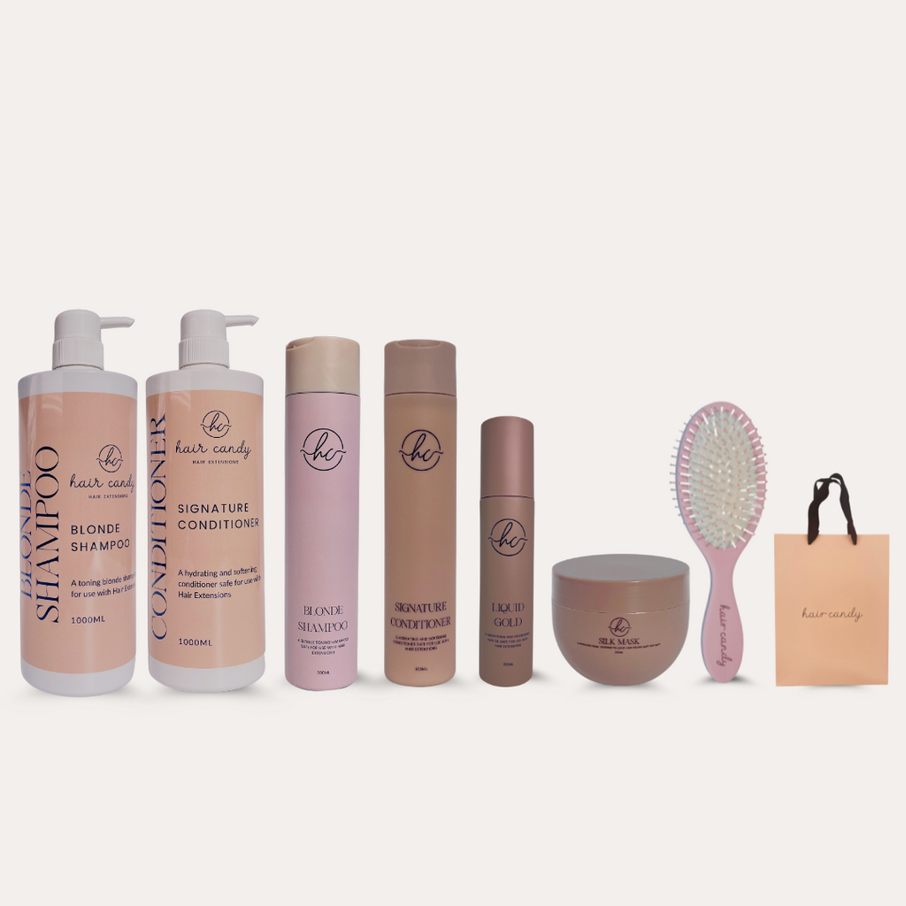 A set of hair care products including shampoo, conditioner, hair oil, silk mask, brushes, and retail bags, predominantly in pink and brown packaging.